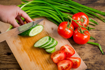 Slicing cucumber on wooden cutting board
