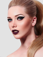 Fototapeta premium Beautiful young blonde with a high tail. Bright makeup, black arrows, purple lips. Beauty salon, spa, hairstyle. In studio on a white background. Advertising cosmetics and hair care products.