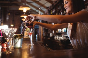 Pretty bartender pouring a cocktail drink in the glass
