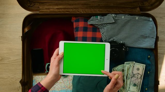 Young woman getting ready for a trip and searching something on tablet with green screen. Chroma key.