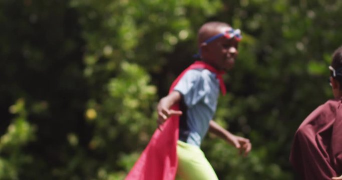 Two young children dressed as superheroes chase each other, slow motion