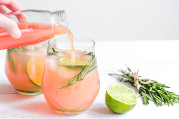 glass of fresh juice with lime and rosemary on white table background