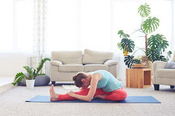 Sportive girl doing head-to-knee forward bend pose on yoga mat