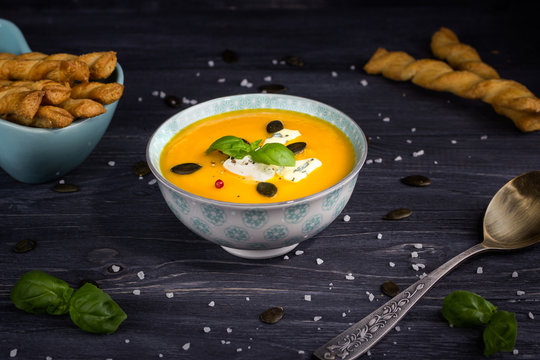 Pumpkin and carrot cream soup with pumpkin seeds and blue cheese on a dark wooden background