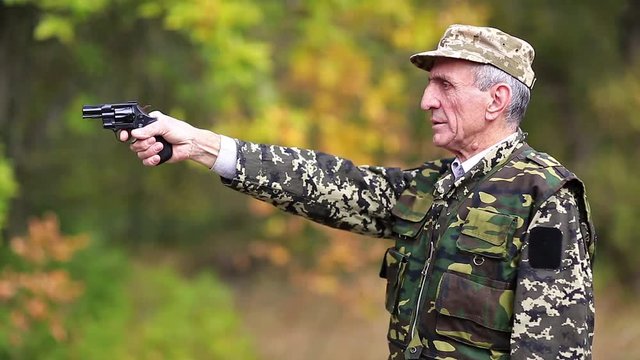 Man with black gun. Senior man in military uniform shoots a revolver. Retired officer at shooting range. Senior man in military uniform shoots a pistol in forest