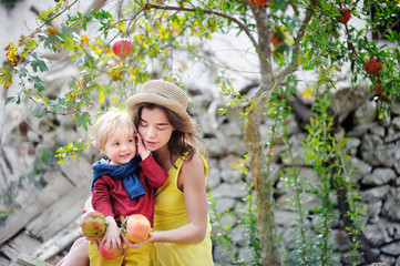 Young woman and cute child picking ripe pomegranate in sunny tree garden in Italy