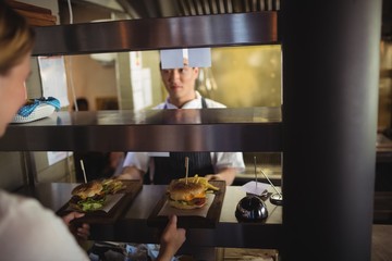 Chef passing tray with French fries and burger to waitress  