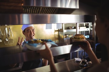 Chef passing tray with french fries and burger to waitress 