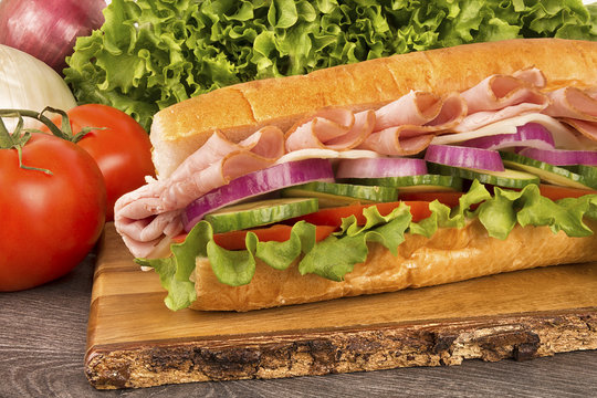 Close up on submarine ham sandwich, vegetables in background.