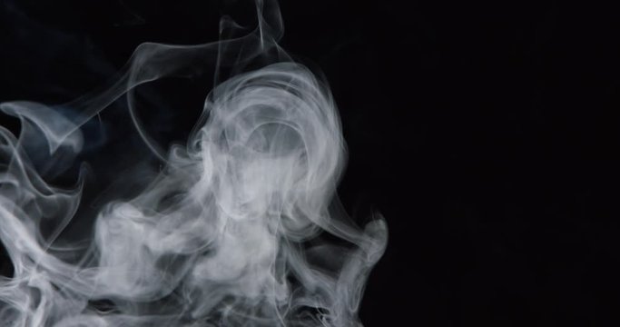 Billows of white turbulent smoke rise through frame against black background