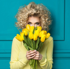 Beautiful blonde girl in yellow shirt with flowers tulips in hands on a turquoise background