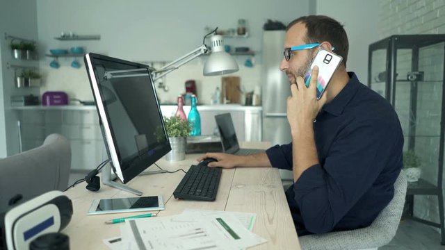 Young man with pc computer talking on cellphone by table at home
