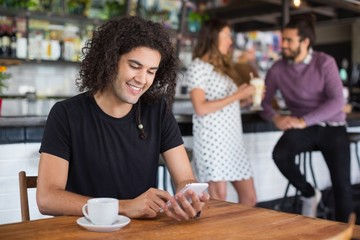 Smiling young man using mobile phone while sitting in restaurant