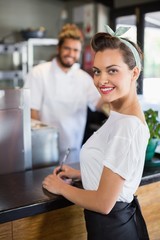 Smiling waitress writing on notepad in kitchen