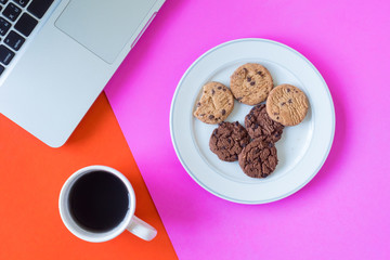 Cookies with coffee cup and laptop on colorful background.