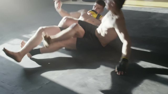 Tracking shot of shirtless MMA fighter performing flying scissor takedown on his opponent during fight, then grappling and throwing punches