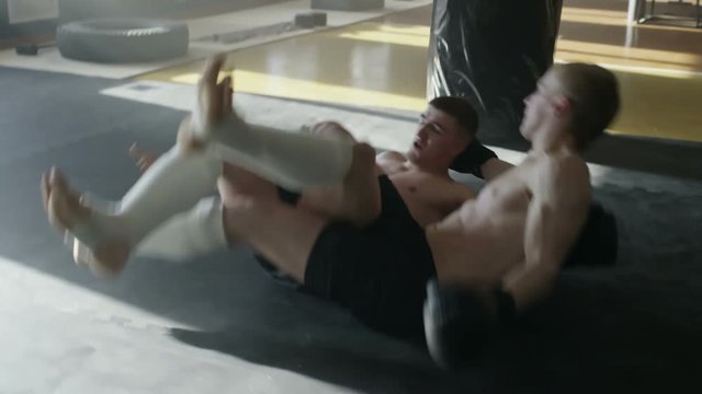 Slow motion of shirtless MMA fighter performing flying scissor takedown on his sparring partner during training, then getting into dominant ground position and getting sweeped 