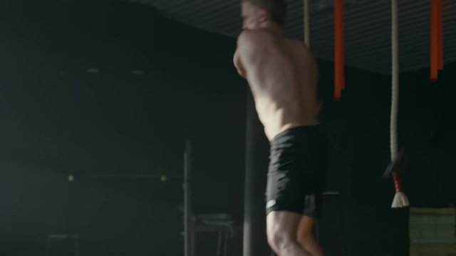 Handheld shot of shirtless athlete swinging sledgehammer overhead and working out in empty gym