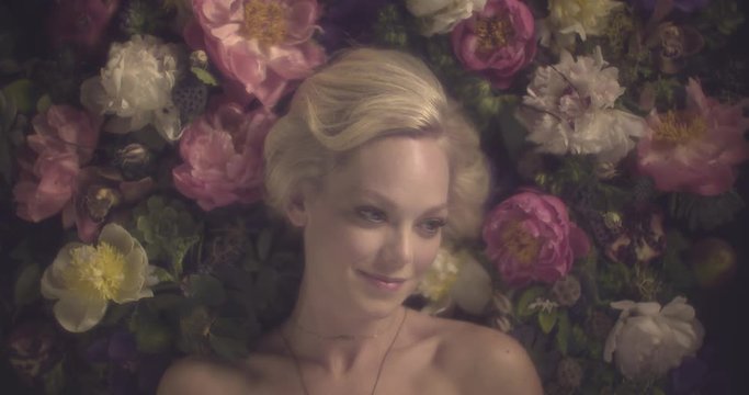 Attractive blonde woman lies in bed of flowers