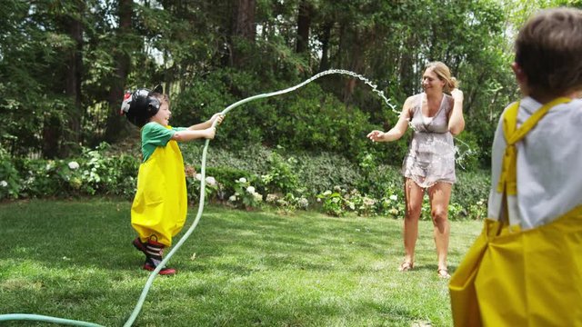 Boy in firefighter costume sprays his mother with a garden hose.