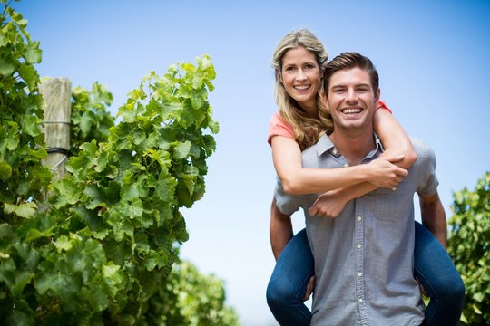 Happy couple piggybacking at vineyard against blue sky