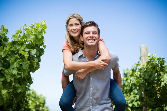 Young couple piggybacking at vineyard against blue sky - Powered by Adobe