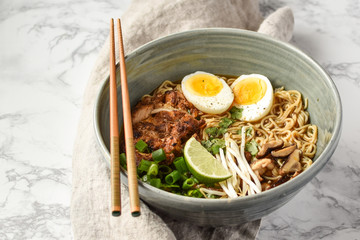 bowl of chicken ramen with chopsticks scallions lime and egg