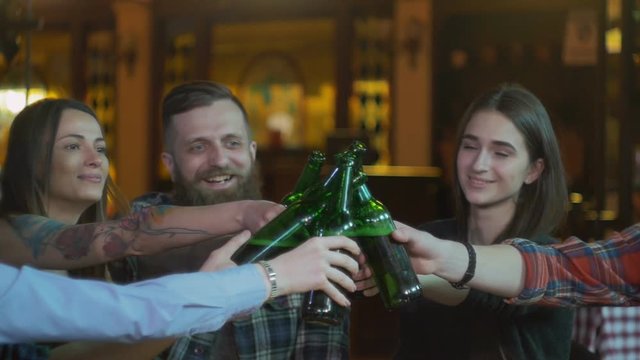 Friends laugh, drink beer and cocktails while having a good time together at a bar. Slow motion