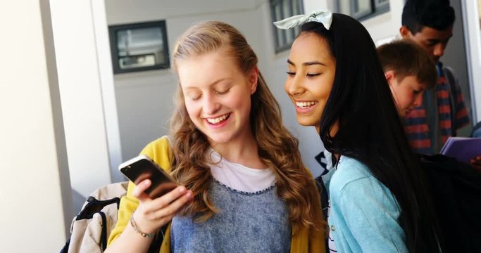  Smiling schoolgirls taking selfie with mobile phone in corridor