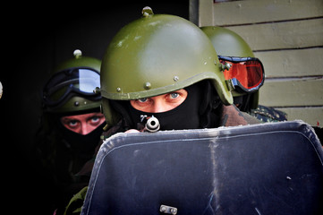 The military man in a helmet and wearing a mask holds a shield and a gun in his hands