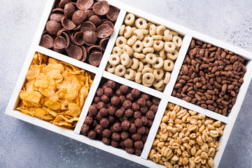 Variety of cold quick breakfast cereals in white wooden box, healthy eating for kids, overhead shot
