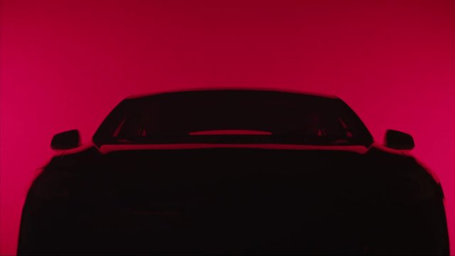 TILT down, silhouette of a sleek car against red background, headlights turn on