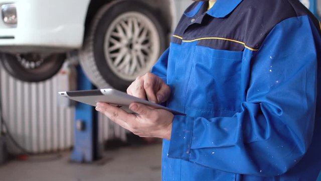 hands of man car mechanic with tablet with lifted car on background