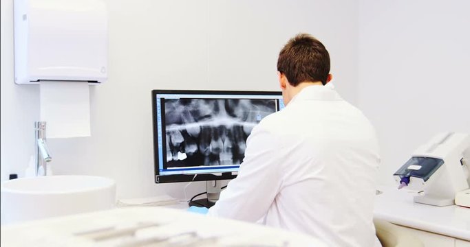 Attentive dentist examining x-ray report on computer