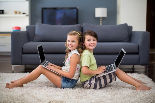 Smiling siblings sitting and using laptop in living