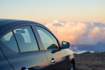 Fototapeta na wymiar Black car in mountains above the clouds at sunset or sunrise