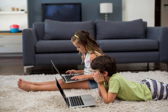 Siblings using laptop in living room
