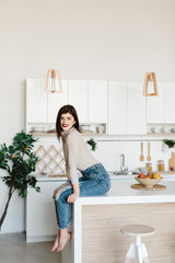 girl sitting on the kitchen table. Bright, white kitchen. Happy smiling girl in the kitchen. Kitchen