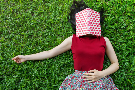Woman lay down on green grass with book in summer