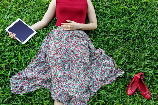Woman lay down and relaxing on green grass, hand holding tablet in Spring or summer time, Top view, Tablet screen is clipping path