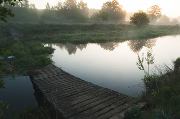 Old dilapidated bridge over a river at dawn,