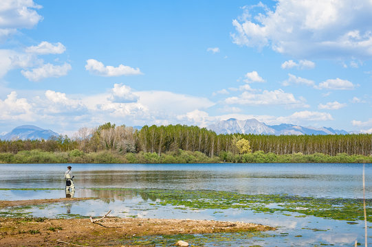 Landscape with man fishing from the shore of lake .
