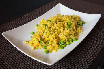 Fried curry rice with peas served on white plate at restaurant, brown background.
