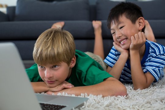 Smiling siblings lying on rug and using laptop in living room - Powered by Adobe