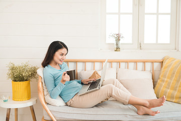 Happy casual beautiful asian young woman working on a laptop at home.