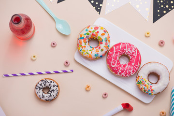 Party. Different colourful sugary round glazed donuts and bottles of drinks on light color background.