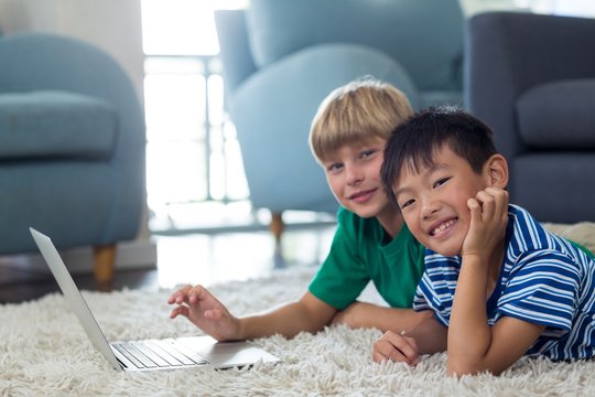 Portrait of siblings lying on rug and using laptop