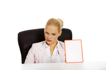 Serious business woman sitting behind the desk and holding board with ban