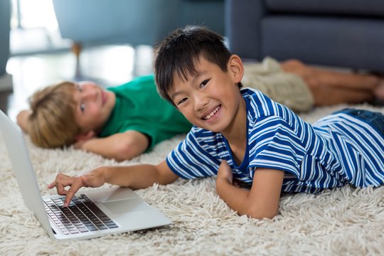 Boy lying on rug and using laptop in living room