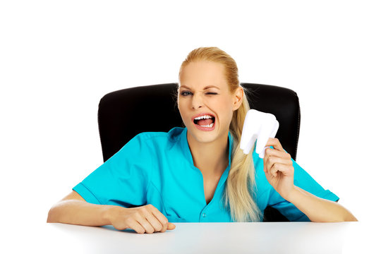 Funny female dentist sitting behing the desk and holding oversized tooth model